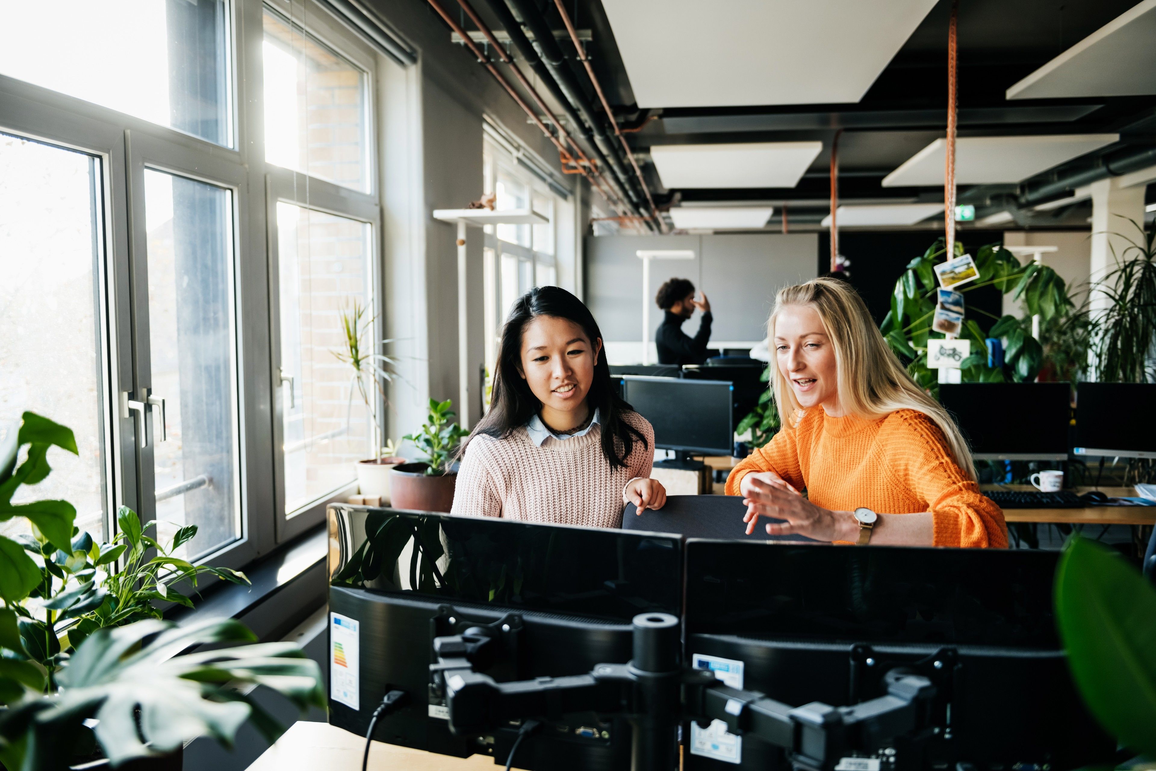 Two people run through sales lead management tools at a desk in their open plan office.